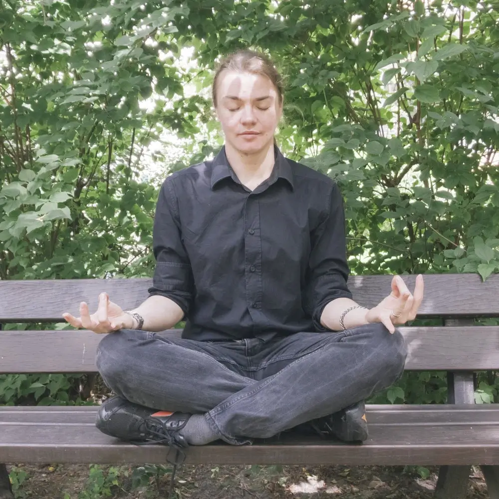 Angel Pretot sits crosslegged on a bench in meditation